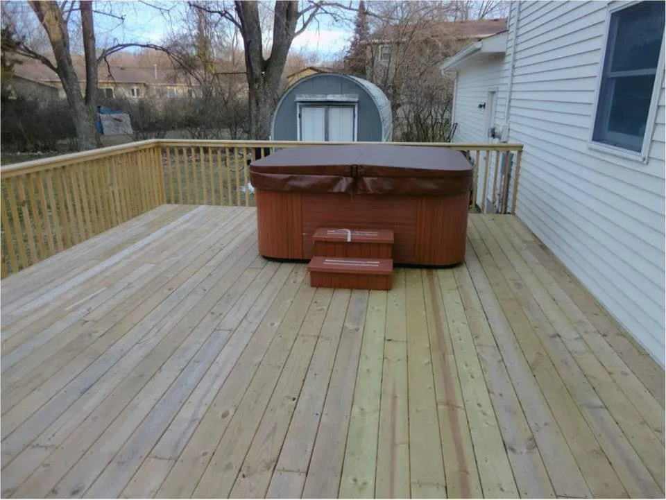 Wooden deck with a hot tub and steps in a residential setting.